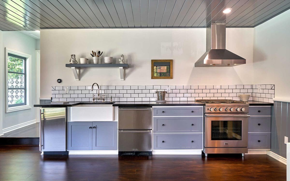 Finished guesthouse kitchen with gray cabinetry, black counters, and subway tile backsplash