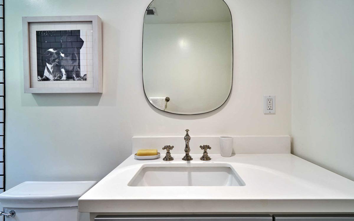 Finished bathroom vanity with white counter and rounded mirror