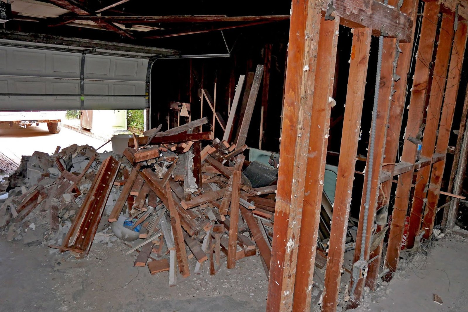 Garage interior during demolition with wall framing exposed and removed materials